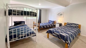 A room with three bunk beds, a wooden chair, a small bedside table with a lamp, and a world map on the wall. - Pirralea (Nelson Bay)