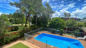 A backyard with a swimming pool, surrounded by a fence, trees, and a grassy area. - Pirralea (Nelson Bay)