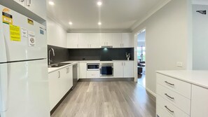 A modern kitchen with white cabinetry, a built-in oven, microwave, and a stainless steel sink.