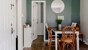 Un coin repas avec une table blanche et des chaises en bois, un miroir rond accroché au mur et une plante en pot posée sur la table.