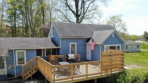 Une maison à deux étages avec une terrasse en bois, un drapeau américain et un barbecue.