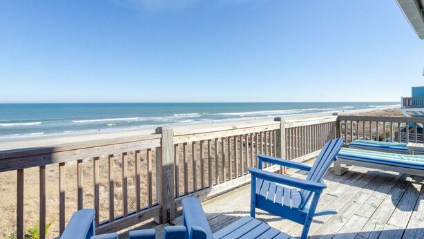 Une terrasse en bois avec des chaises bleues donnant sur une plage.