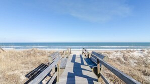 Une promenade en bois menant à une plage où se trouvent des bancs.