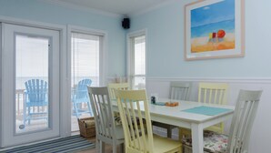 Un coin repas avec une table et des chaises blanches, un tableau au mur et une vue par la fenêtre.