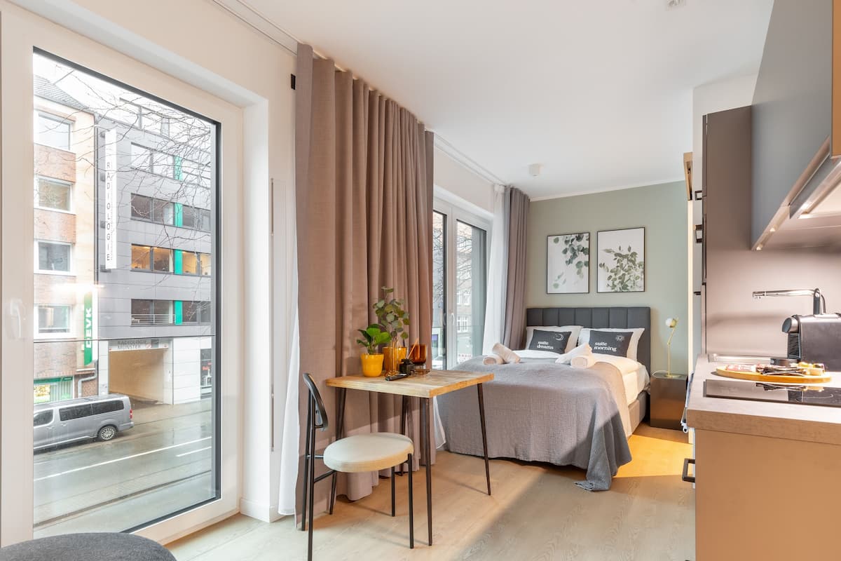 Quarto de hotel moderno com cama, escrivaninha e uma janela grande.