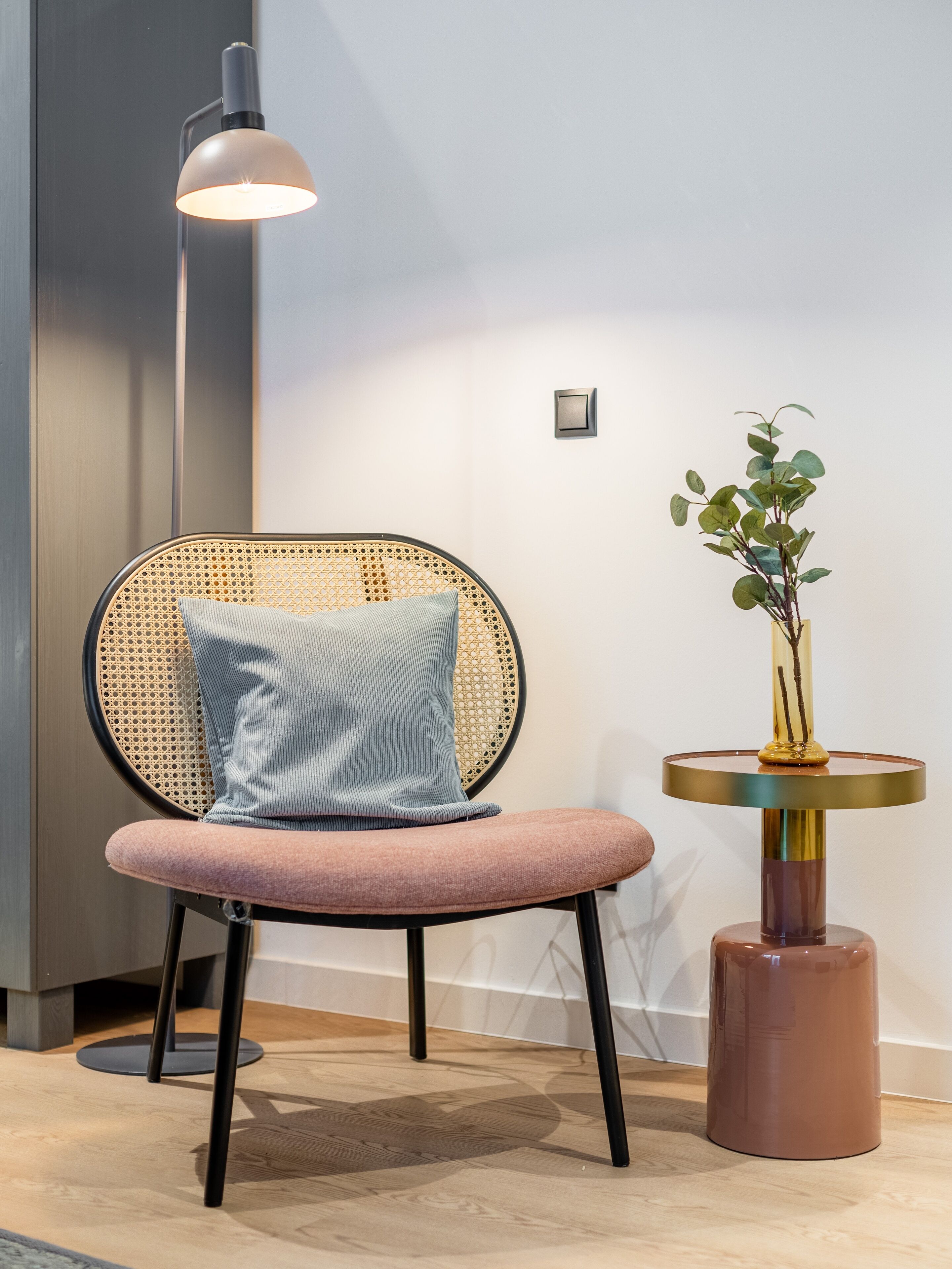 A modern chair with a rattan backrest and a cushion, a floor lamp, and a small table with a plant.
