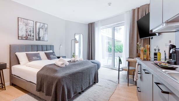 A modern hotel room with a large bed, a flat-screen TV, a kitchenette, and a sliding glass door to the outside. - Limehome Münster Von-Steuben-Str. (Münster)