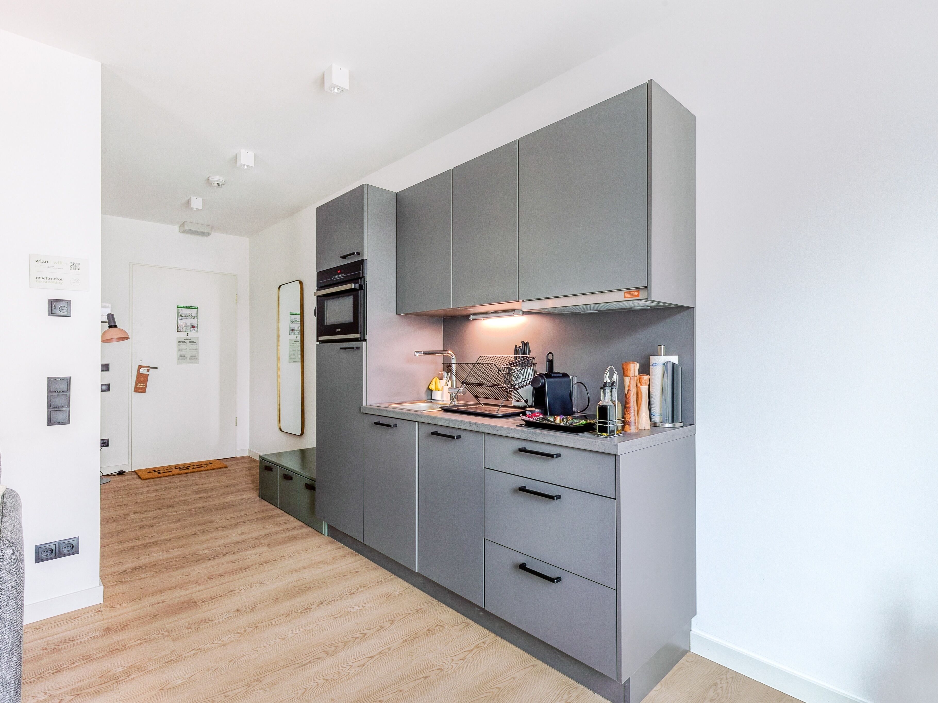 A modern kitchen with grey cabinets, a built-in oven, and a stainless steel sink.