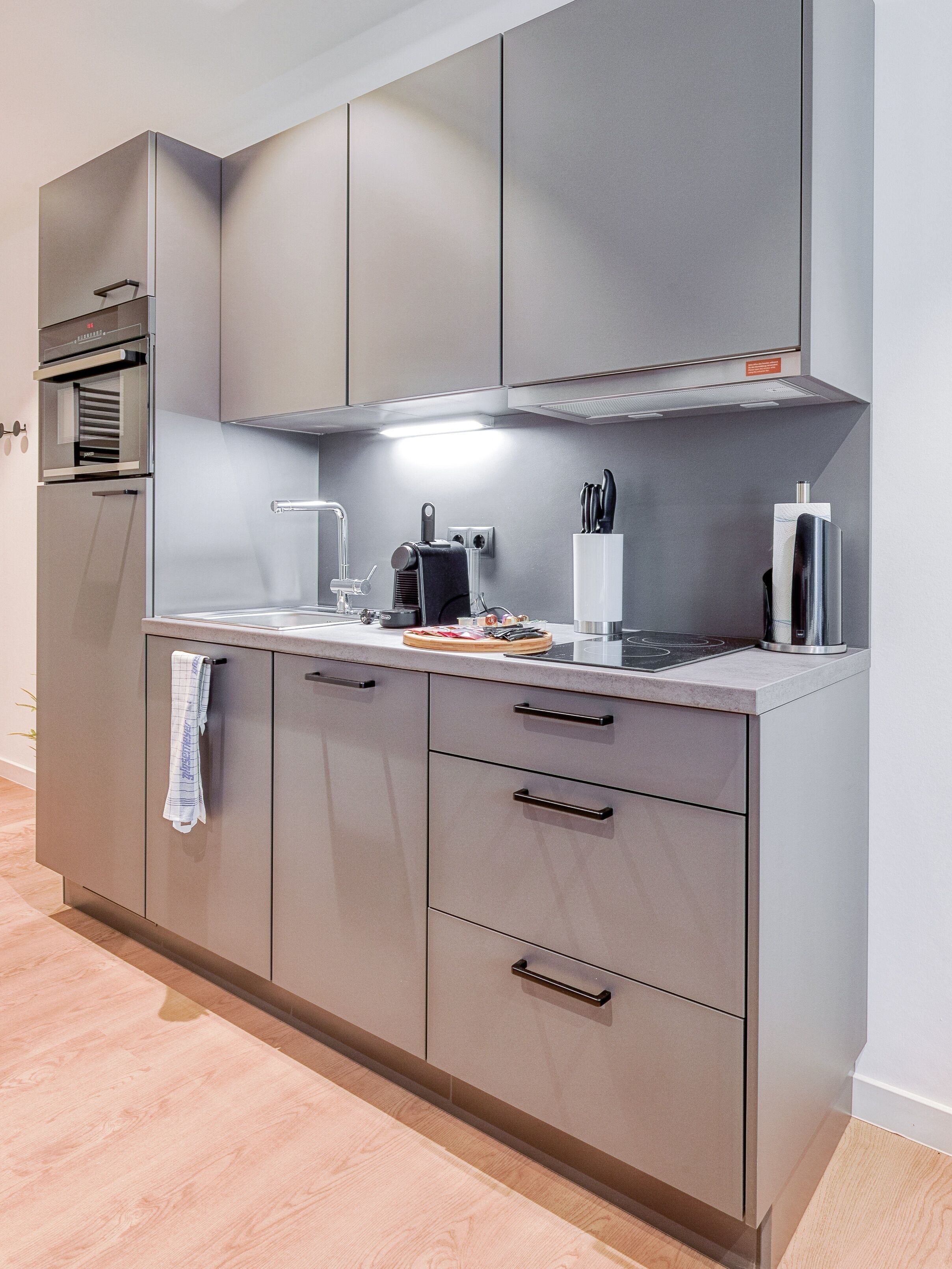 A modern kitchen with grey cabinets, a built-in oven, and a stainless steel range hood.