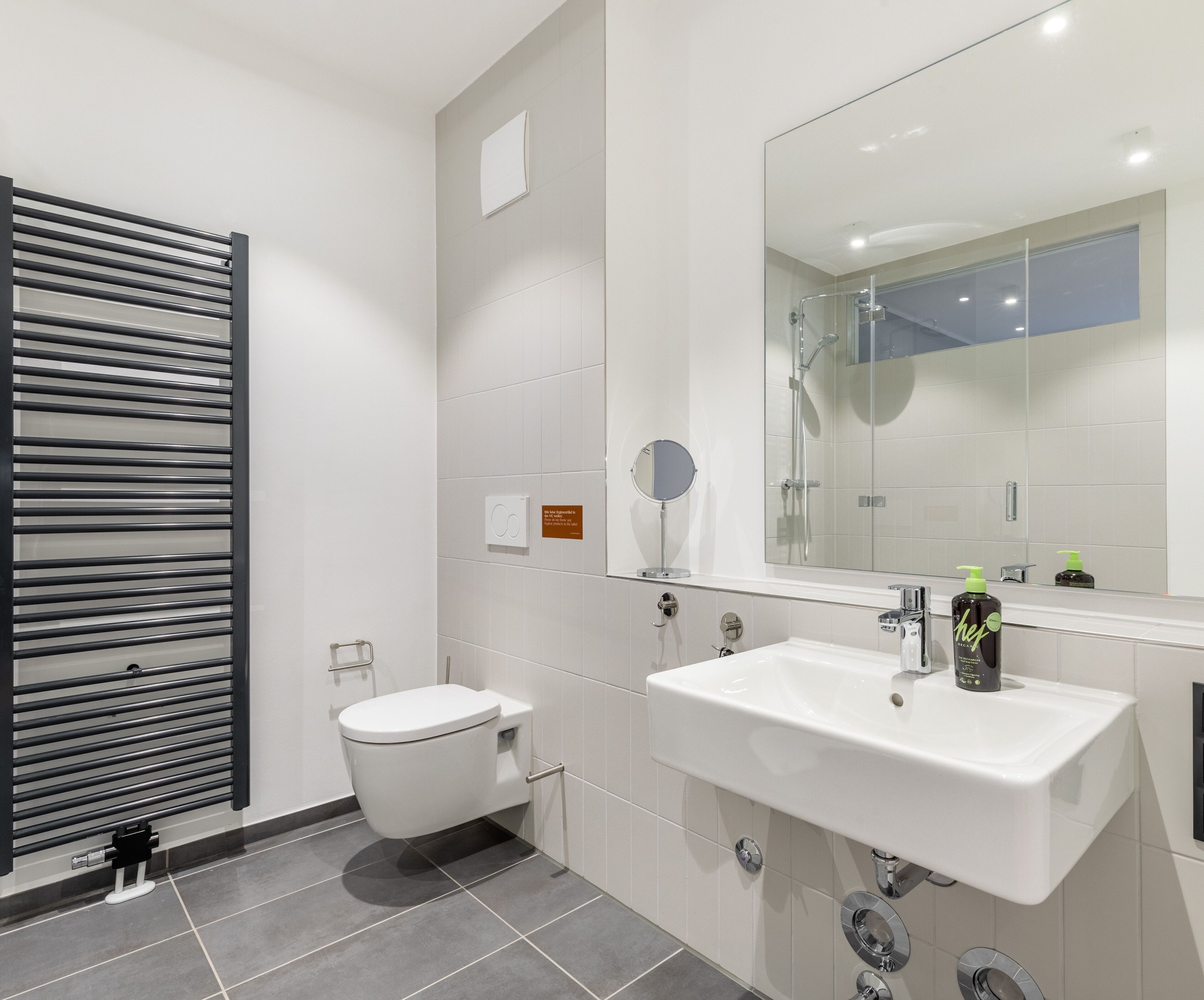 Une salle de bain moderne équipée de toilettes, d’un grand miroir, d’un lavabo et d’une douche.