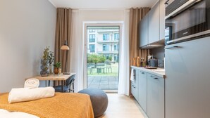 A modern hotel room with a bed, a desk, a kitchenette, and a view of the outdoor patio. - Limehome Münster Von-Steuben-Str. (Münster)