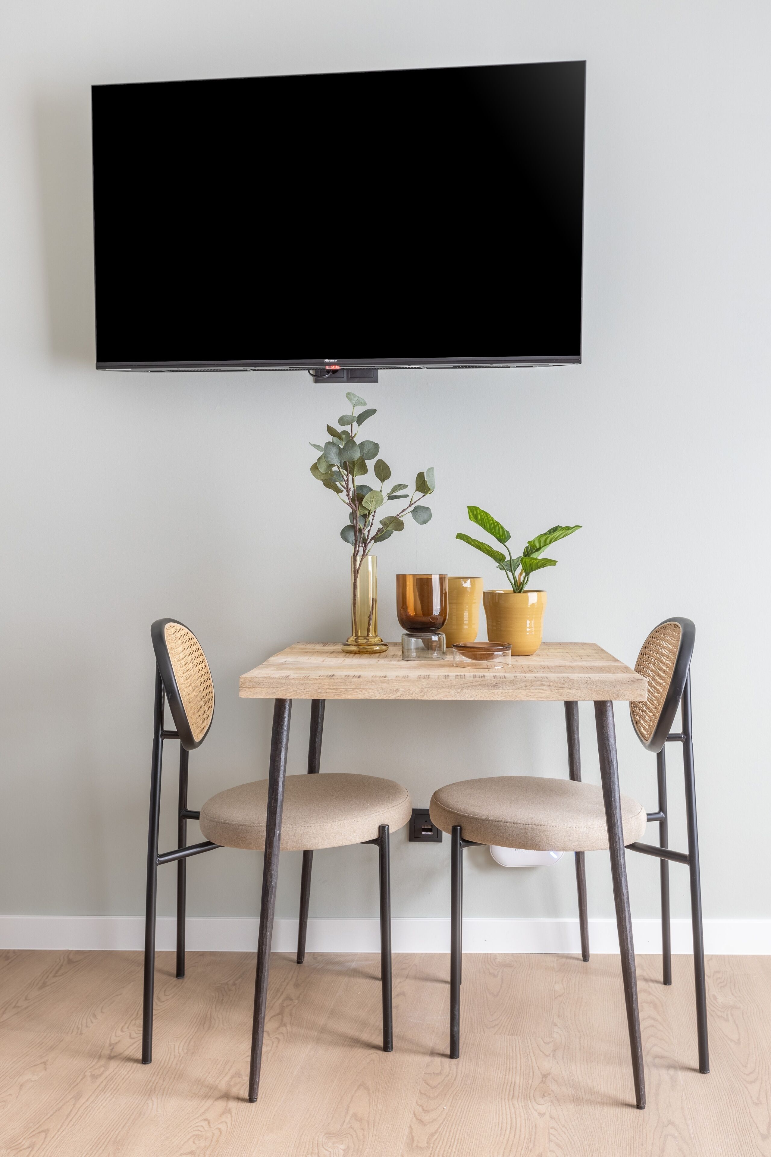 A dining area with a table, chairs, a flat-screen TV, and decorative plants.