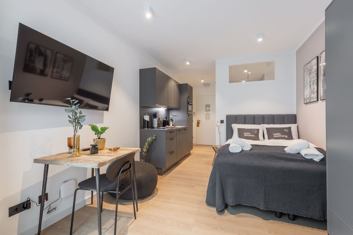 Quarto de hotel moderno com cama, escrivaninha e cozinha compacta.