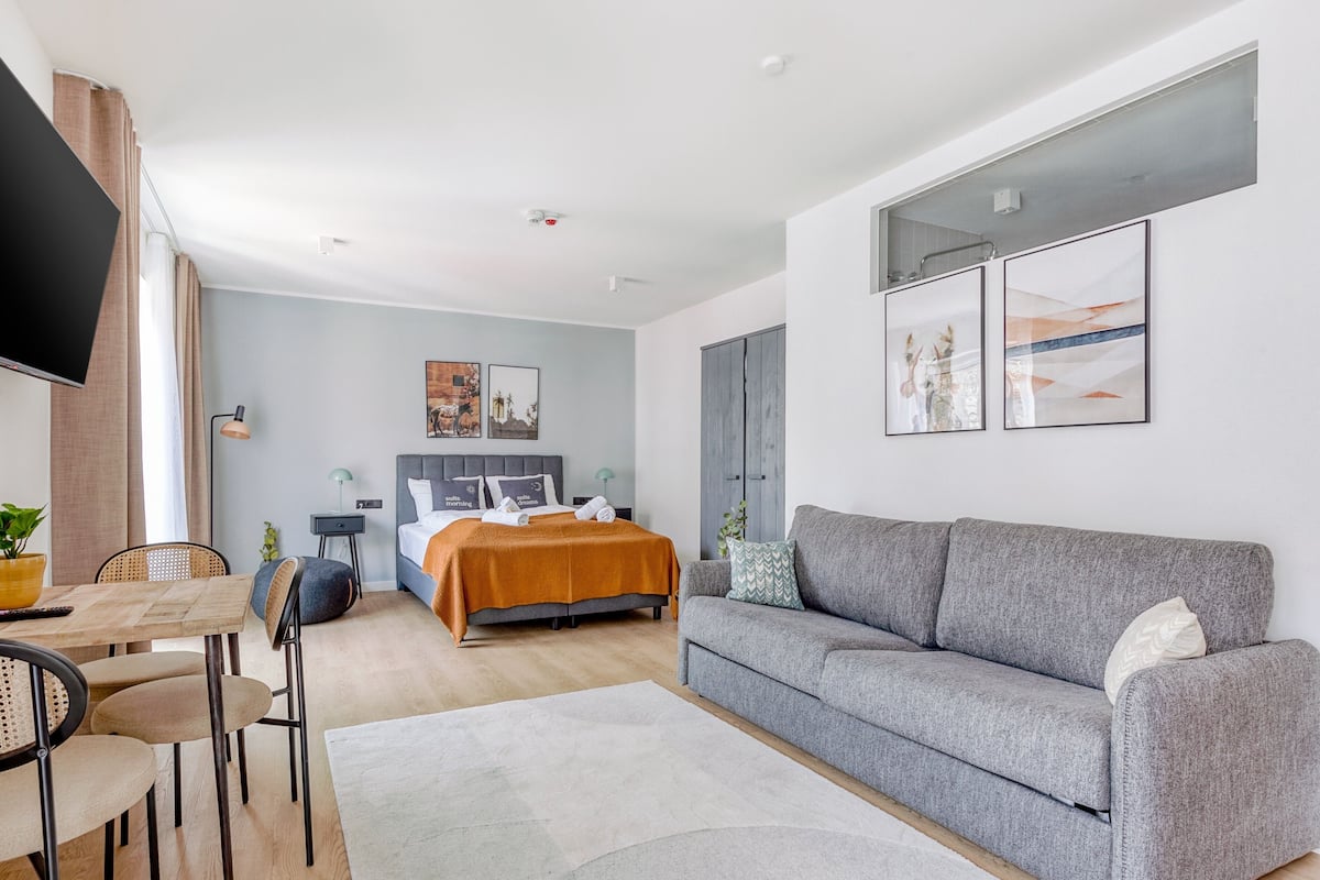 Quarto de hotel moderno com cama, sofá, área de refeições e TV.
