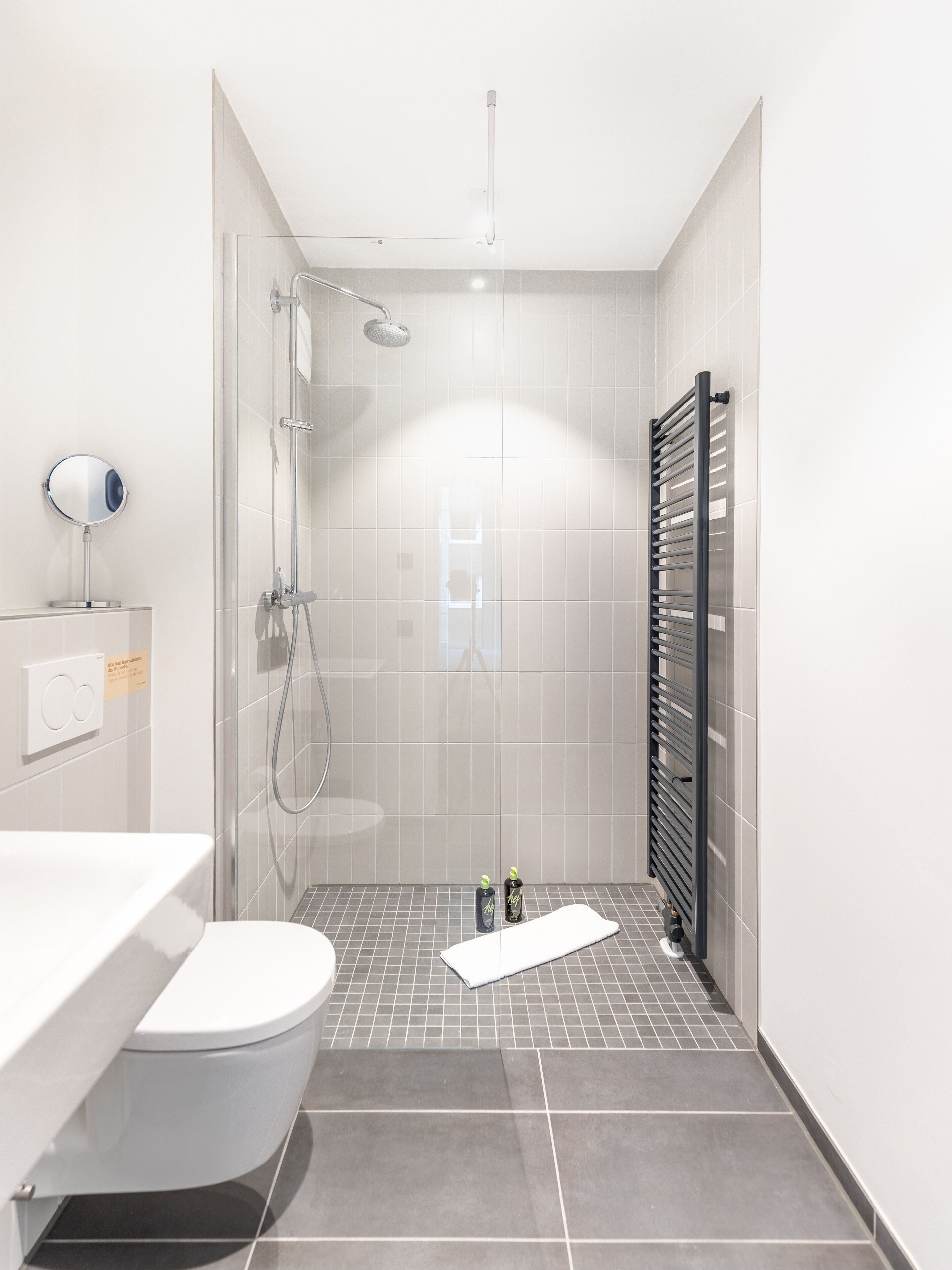 A modern bathroom with a shower, toilet, and a towel rack.