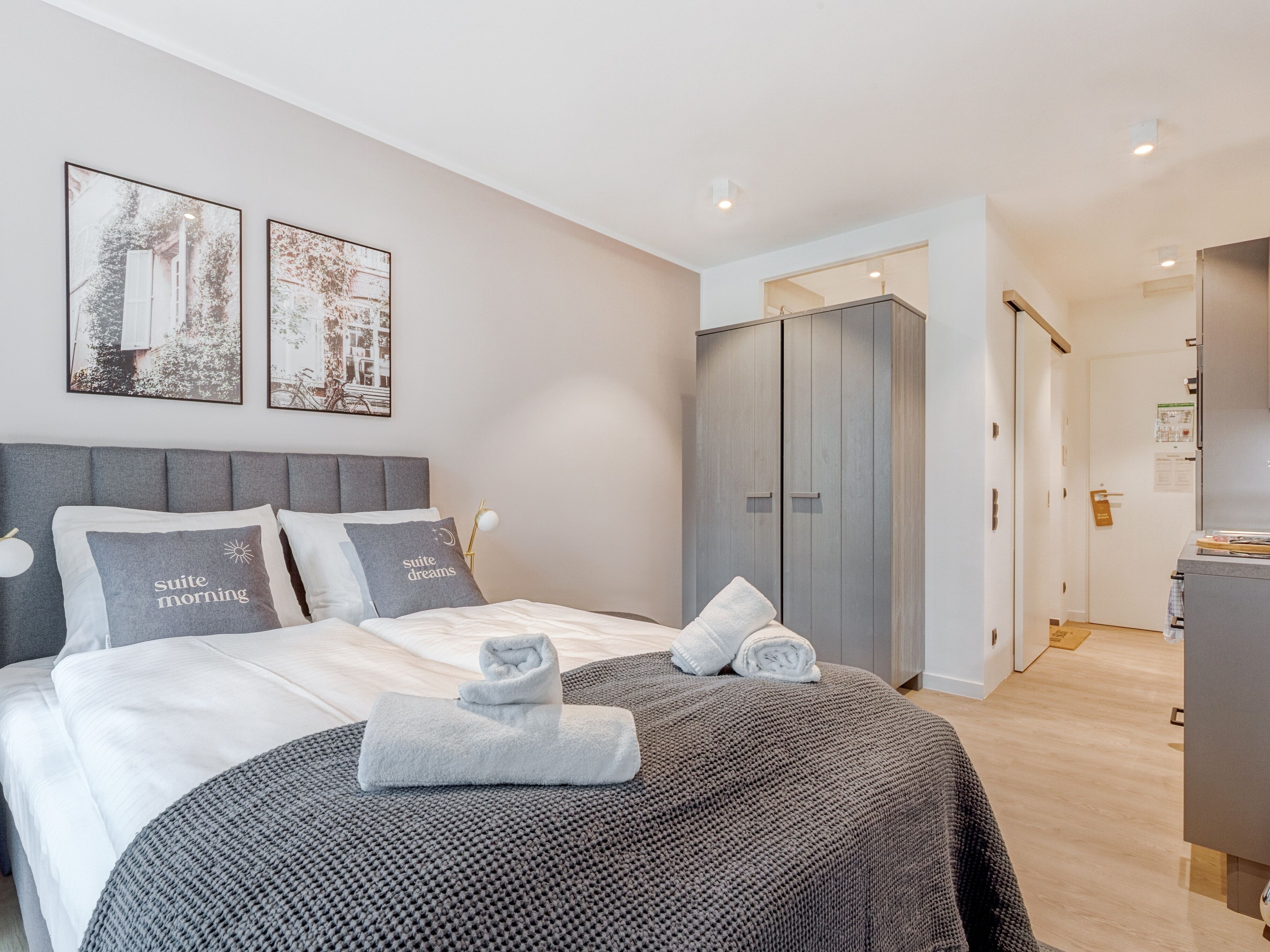 Ein modernes Schlafzimmer mit einem Bett, grauer Bettwäsche, zwei Kissen, einer grauen Strickdecke und einem grauen Kleiderschrank.