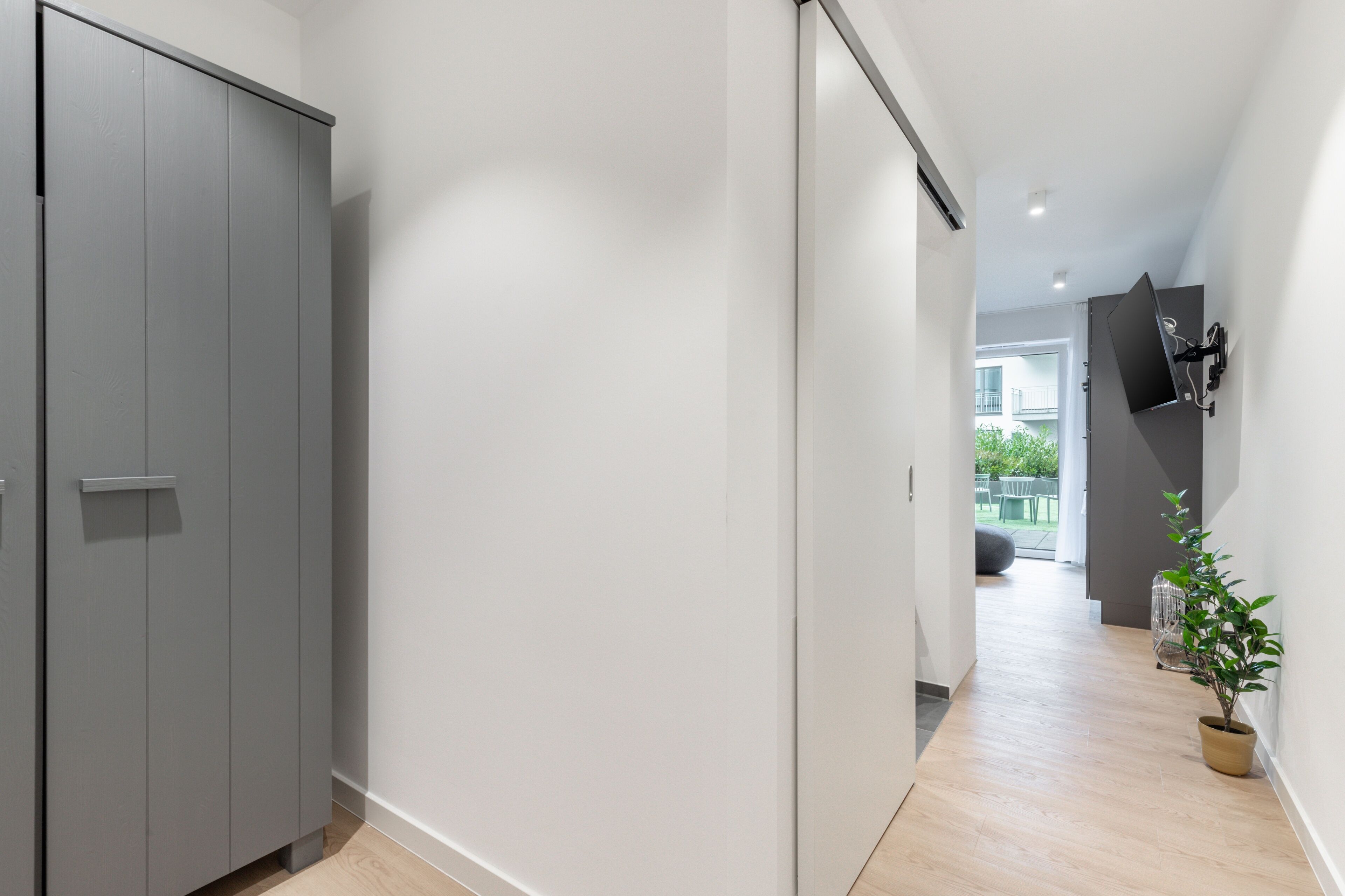 A hallway with a grey wardrobe, a potted plant, and a mounted TV.