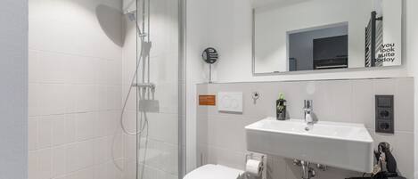 A modern bathroom with a glass shower enclosure, a white toilet, and a sink with a mirror above it.