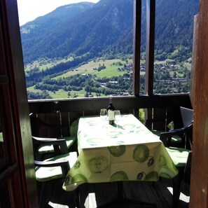 A table with a tablecloth, chairs, and a bottle of wine on a balcony overlooking a valley with mountains in the background. - Chalet-Schümli Maisonette Dream view of the Aletsch Arena, hiking, skiing, bike  (Ernen)