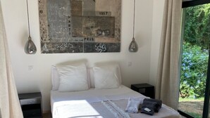 Ein Schlafzimmer mit einem großen Bett, Holzboden, einem Nachttisch und Blick ins Grüne durch ein Fenster.
