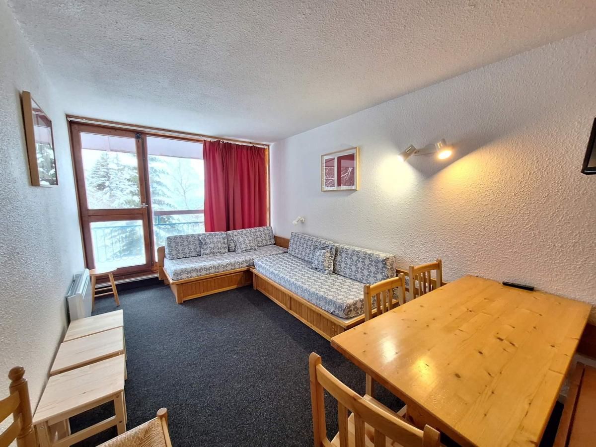 Tunnelmallinen huone, jossa on puinen pöytä, sohva ja pieni ikkuna, jossa on punaiset verhot.