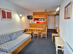 A compact living space with a sofa, a dining table with chairs, a kitchenette area with a microwave, and a television.