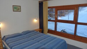 Een slaapkamer met een bed, een nachtkastje, een raam met uitzicht op een besneeerd landschap en een wandlamp.
