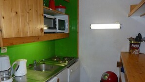 Een kleine keuken met een magnetron, kookplaat, gootsteen en koffiezetapparaat.