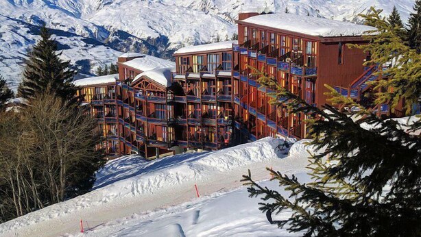 Een meerlaags hotel met een houten gevel en balkons, gelegen voor een besneeuwd berglandschap.