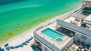 A rooftop pool with clear blue water, surrounded by beach umbrellas and lounge chairs, overlooking a sandy beach and turquoise sea. - Ocean Front with Rooftop Pool Access (Destin)