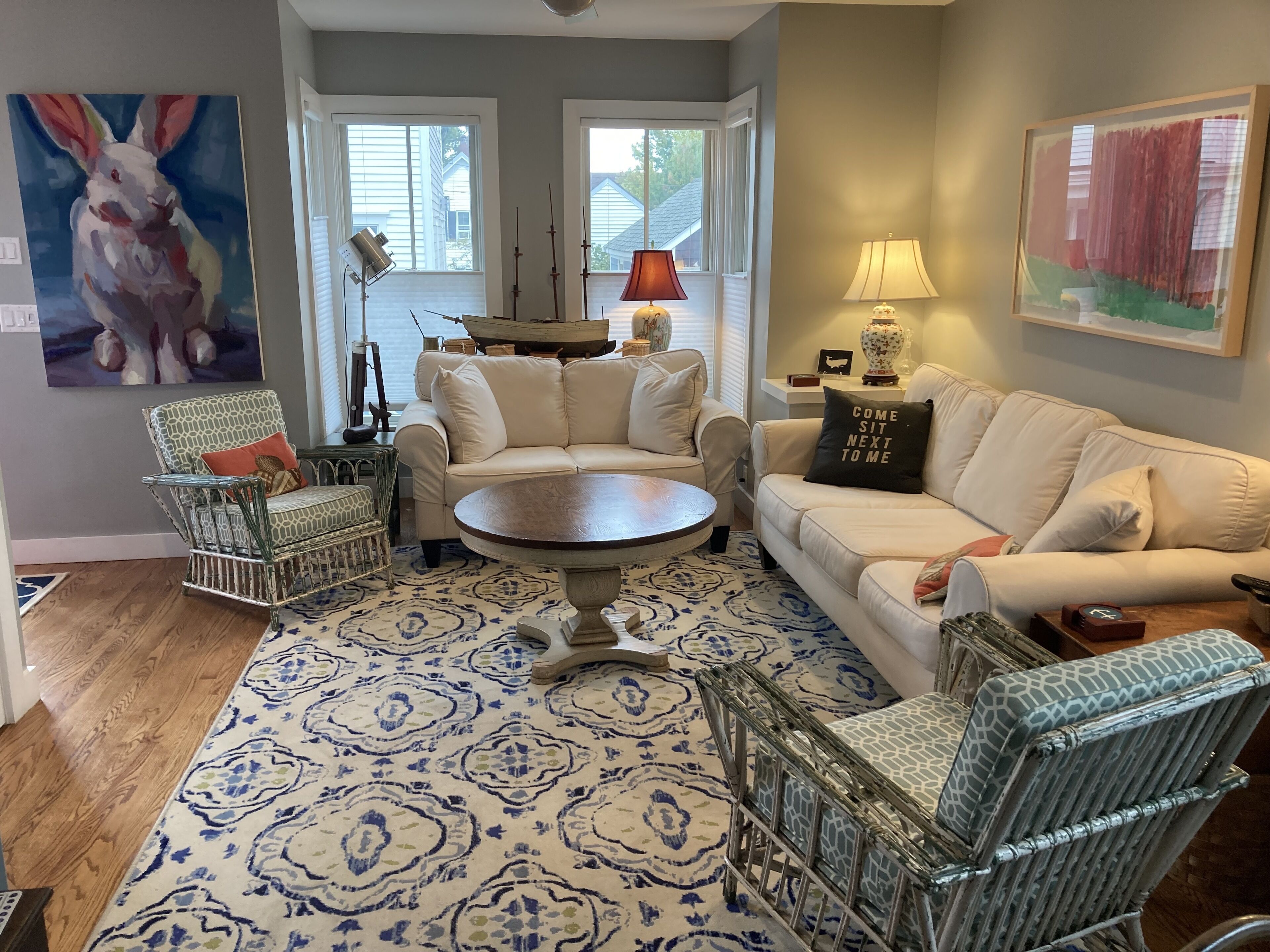 A living room with a patterned rug, a white sofa, a patterned armchair, a round coffee table, and a painting of a rabbit.