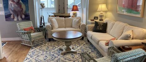 A living room with a patterned rug, a white sofa, a patterned armchair, a round coffee table, and a painting of a rabbit.