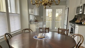 Une table de salle à manger ronde en bois, entourée de chaises, un lustre et une vue sur le jardin à travers une porte coulissante.