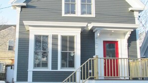 Une maison à deux étages avec une porte rouge, des boiseries blanches et un petit porche à l’avant.