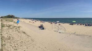 A beach with people sunbathing and swimming, a lifeguard tower, and a clear blue sky.