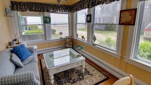 A cozy living room with a checkered sofa, a glass coffee table, and a view of the street through large windows.