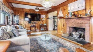 A cozy living room with a fireplace, wooden walls, a television, and a chandelier.