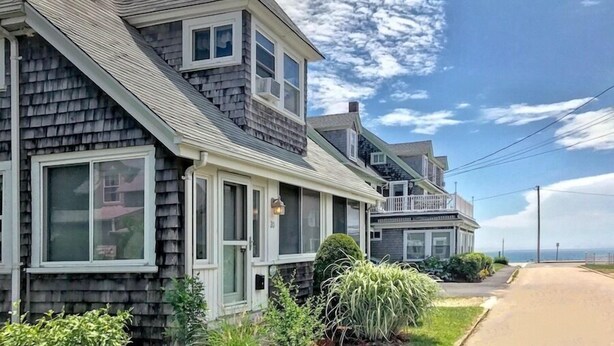 A row of two-story houses with a sloped roof, large windows, and a small porch.