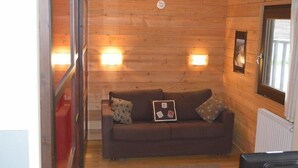 A cozy room with a wooden wall, a brown sofa with cushions, and two wall-mounted lights.