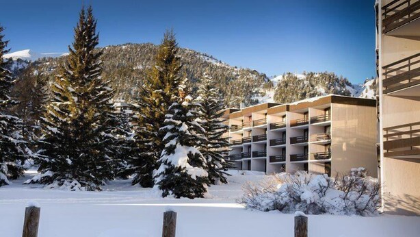 A snow-covered parking area with a modern building featuring multiple balconies.