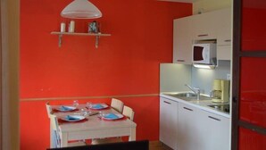 A compact kitchen with white cabinets, a microwave, and a sink. There is a dining table set with plates and glasses.