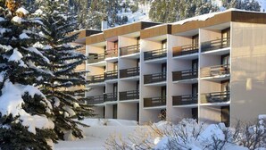 A multi-story building with balconies, surrounded by snow-covered trees and shrubs.