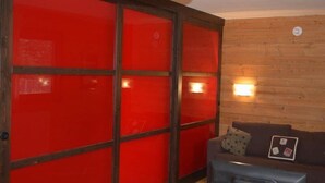 A room with a red sliding door, a wooden wall, a brown sofa with cushions, and a television.