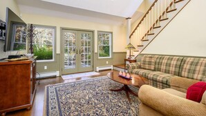 A spacious living room with a large window, a staircase, and a cozy sofa. - Large Chatham Rental w/ 5 Bedrooms w/ 5 Private Bathrooms RPAM007 (Chatham)