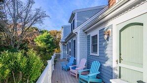A house with a porch featuring four Adirondack chairs in pastel colors. - Large Chatham Rental w/ 5 Bedrooms w/ 5 Private Bathrooms RPAM007 (Chatham)