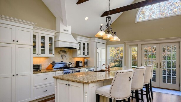 A spacious kitchen with white cabinetry, a large island with bar stools, and a hanging light fixture. - Large Chatham Rental w/ 5 Bedrooms w/ 5 Private Bathrooms RPAM007 (Chatham)