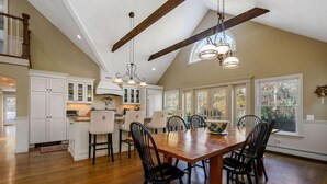 A spacious kitchen with a large wooden table and chairs, white cabinetry, and a vaulted ceiling with exposed beams. - Large Chatham Rental w/ 5 Bedrooms w/ 5 Private Bathrooms RPAM007 (Chatham)