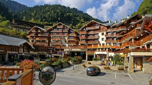 A multi-story hotel with balconies, a parking area, and a mountainous backdrop. - 50m from ski slopes, 3rd floor, view village, balcony, tv, 23m², Champagny-en-Vanoise (Champagny-en-Vanoise)
