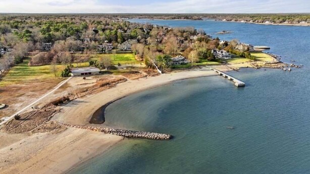An aerial view of a coastal area with a sandy beach, a pier, and houses along the shoreline.