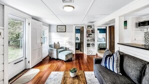 A spacious living room with hardwood flooring, a grey sofa, a coffee table with a plant, and a bookshelf.